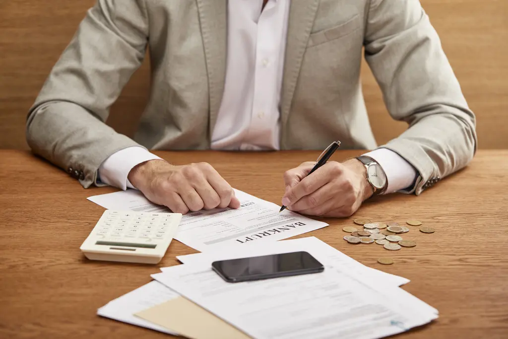 Man reviewing and signing bankruptcy documents with calculator, coins, and paperwork on desk, representing Chapter 7 and Chapter 13 debt relief options.