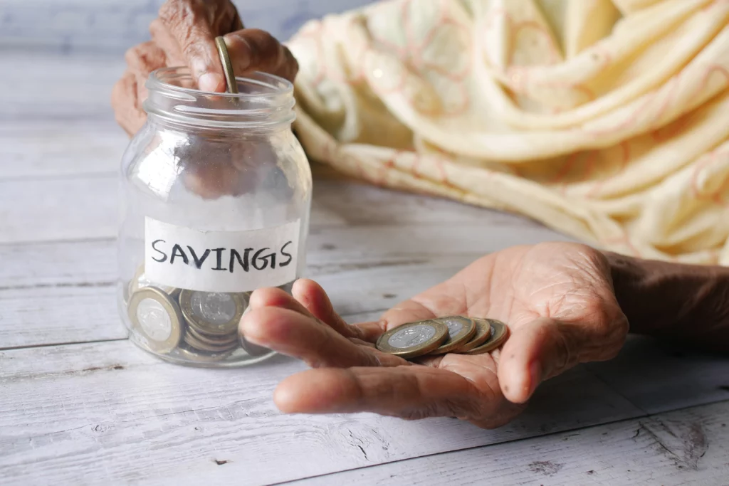 Elderly person holding coins beside a jar labeled “savings,” representing protecting retirement funds during bankruptcy.