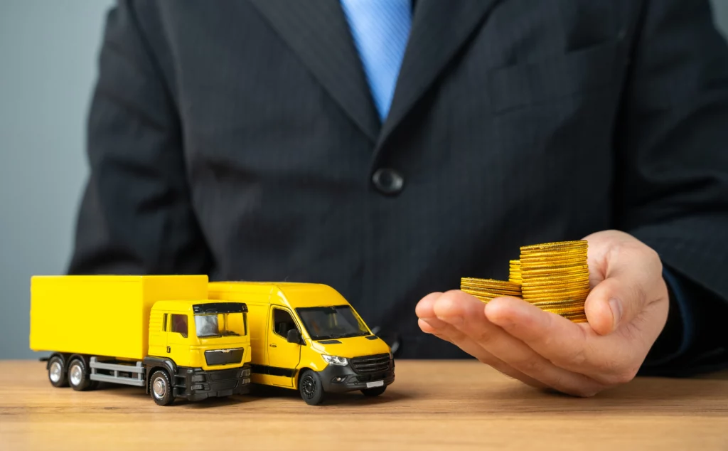 Person in suit holding gold coins next to toy truck and van — symbolizing business vehicle investment.